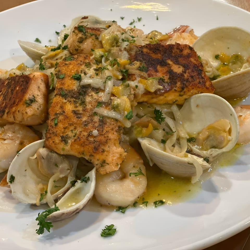 Grilled salmon and shrimp with clams, scallops, onions, peppers, and parsley in a light seafood sauce.